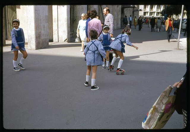 Four girls in matching outfits, one has strap-on roller skates